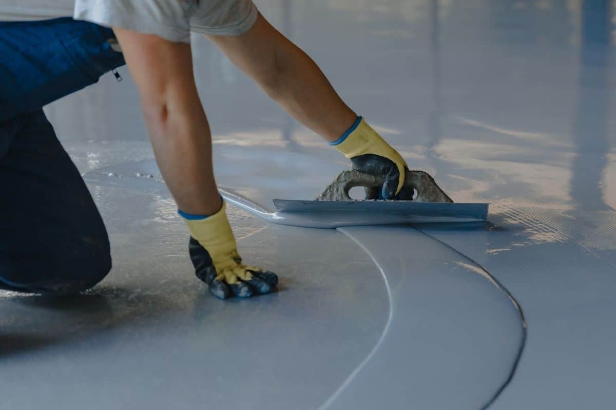 a man applying grey epoxy resin to a garage floor